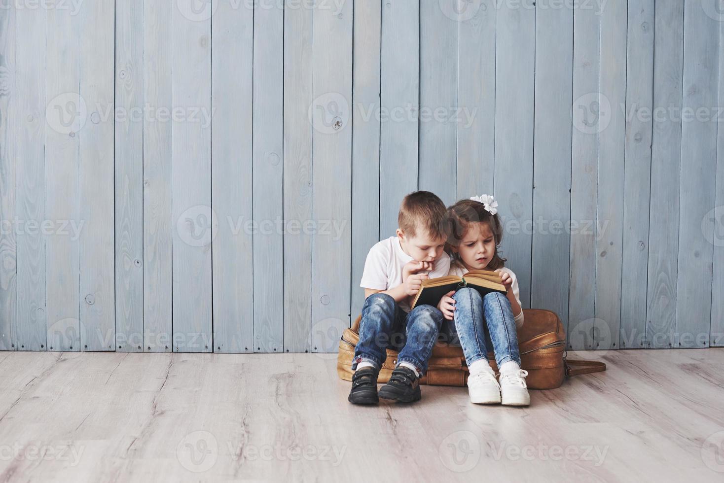 listo para grandes viajes. feliz niña y niño leyendo un libro interesante con un maletín grande y sonriendo. concepto de viaje, libertad e imaginación. foto