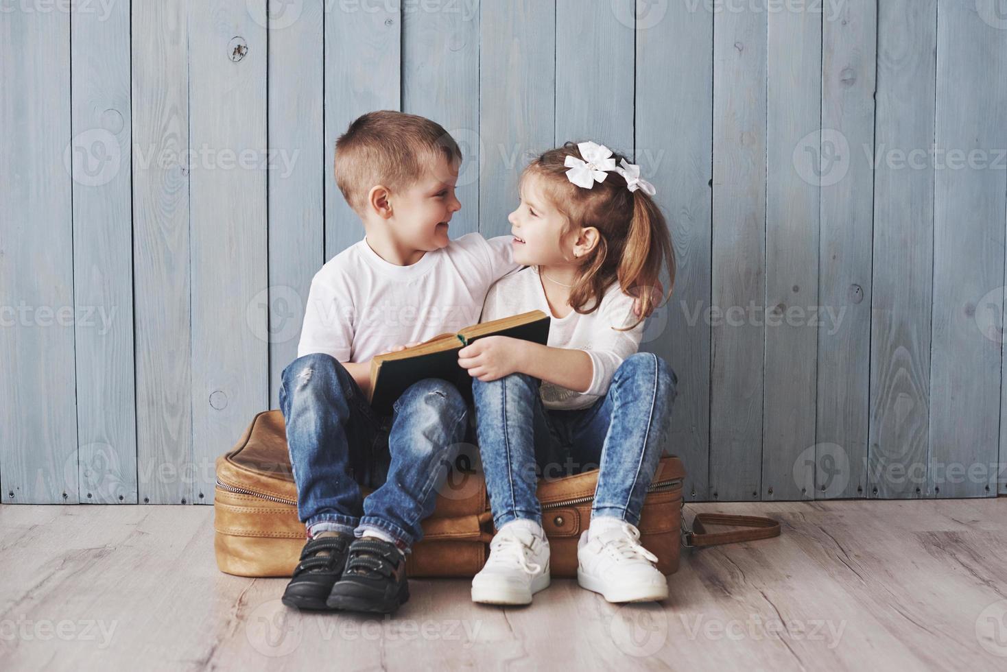 Ready to big travel. Happy little girl and boy reading interesting book carrying a big briefcase and smiling. Travel, freedom and imagination concept photo