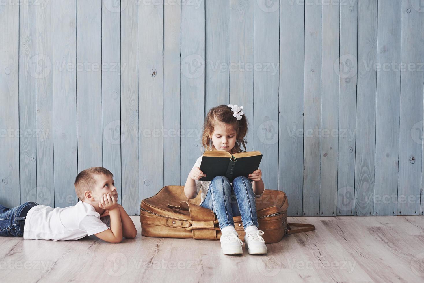 listo para grandes viajes. feliz niña y niño leyendo un libro interesante con un maletín grande y sonriendo. concepto de viaje, libertad e imaginación. foto