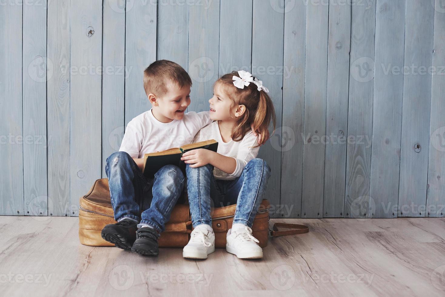 listo para grandes viajes. feliz niña y niño leyendo un libro interesante con un maletín grande y sonriendo. concepto de viaje, libertad e imaginación. foto