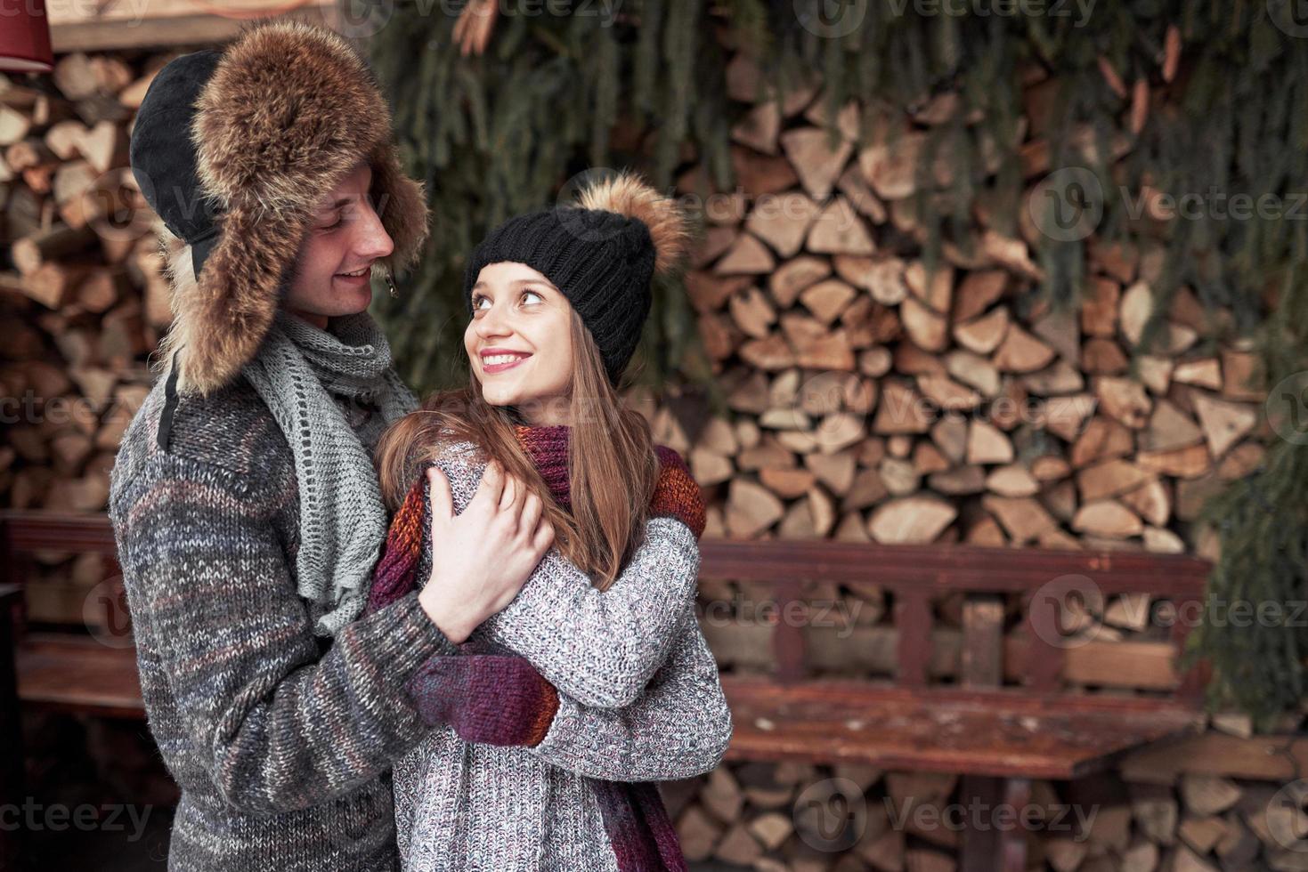 winter, vacation, couple, christmas and people concept - smiling man and woman in hats and scarf hugging over wooden country house and snow background photo