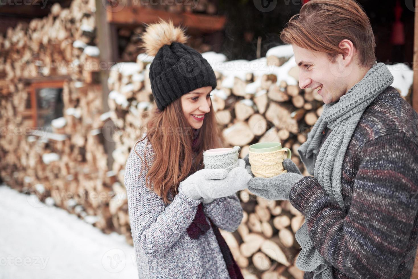 Photo of happy man and pretty woman with cups outdoor in winter. Winter holiday and vacation. Christmas couple of happy man and woman drink hot wine. Couple in love