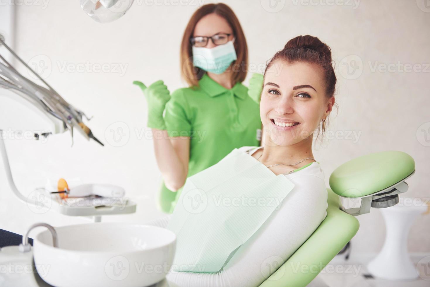 A young woman is satisfied with the work of the dentist and holds up her thumb photo