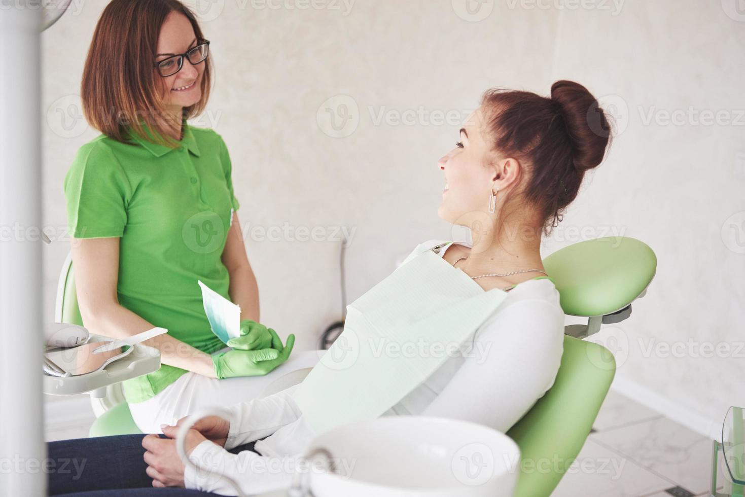 Dentista en el consultorio dental hablando con la paciente y preparándose para el tratamiento foto