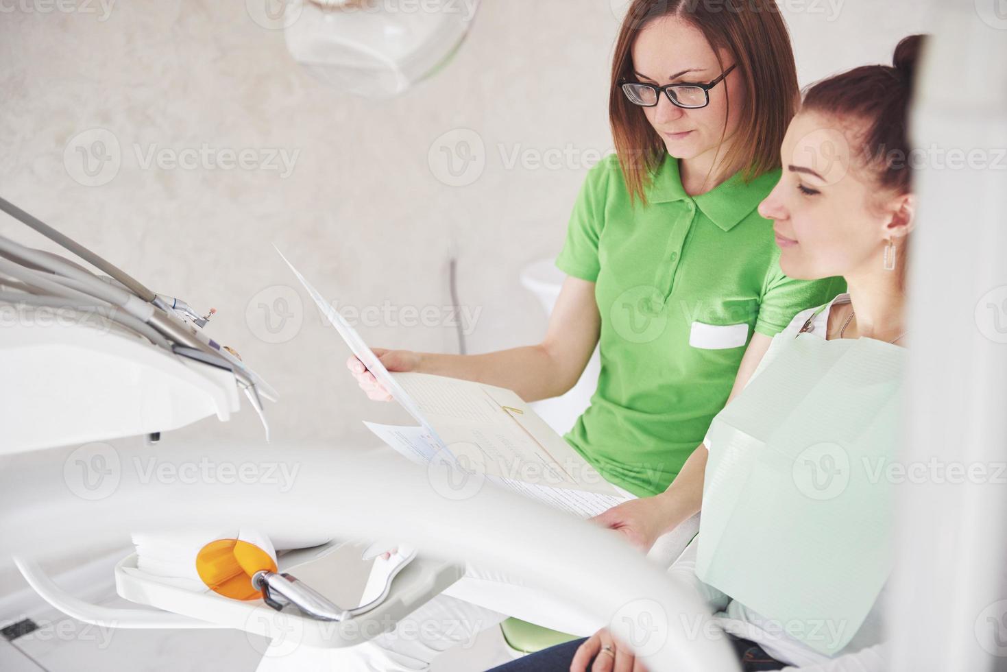 Dentista en el consultorio dental hablando con la paciente y preparándose para el tratamiento foto