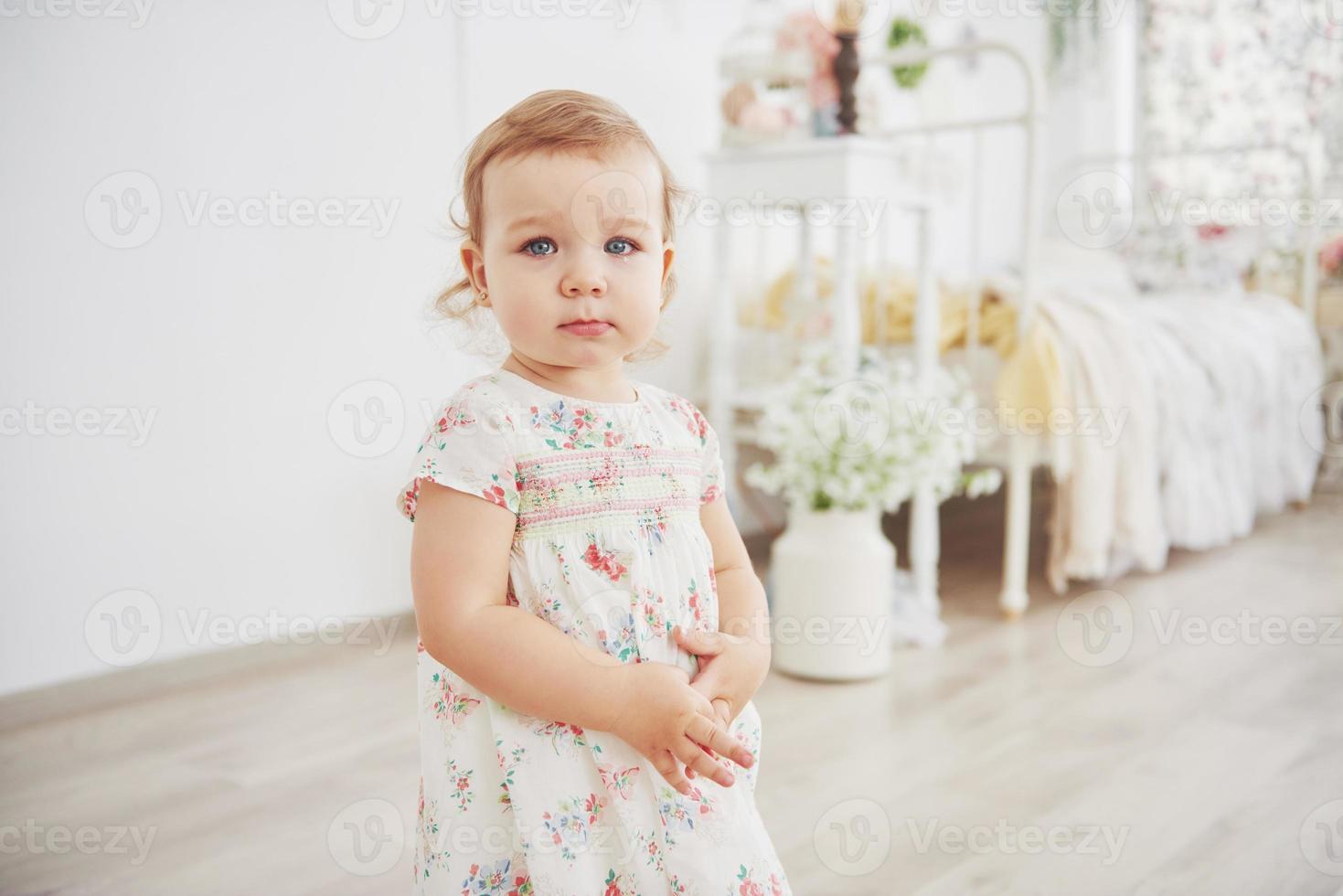 hermosa niña jugando juguetes. rubia de ojos azules. silla blanca. cuarto de los niños. retrato de niña pequeña feliz. concepto de infancia foto