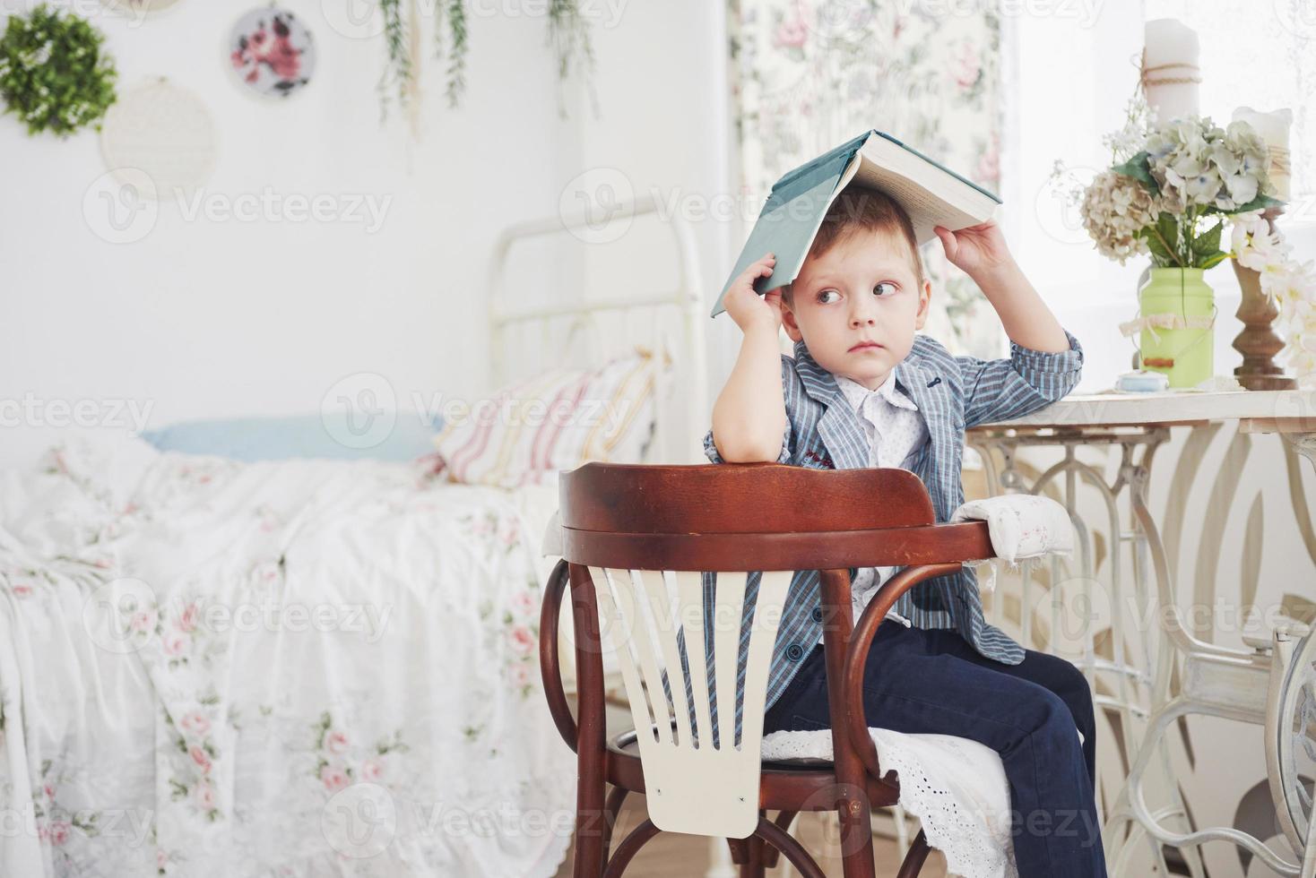 Photo of diligent schoolboy with book on his head doing homework. The schoolboy is tired of doing homework