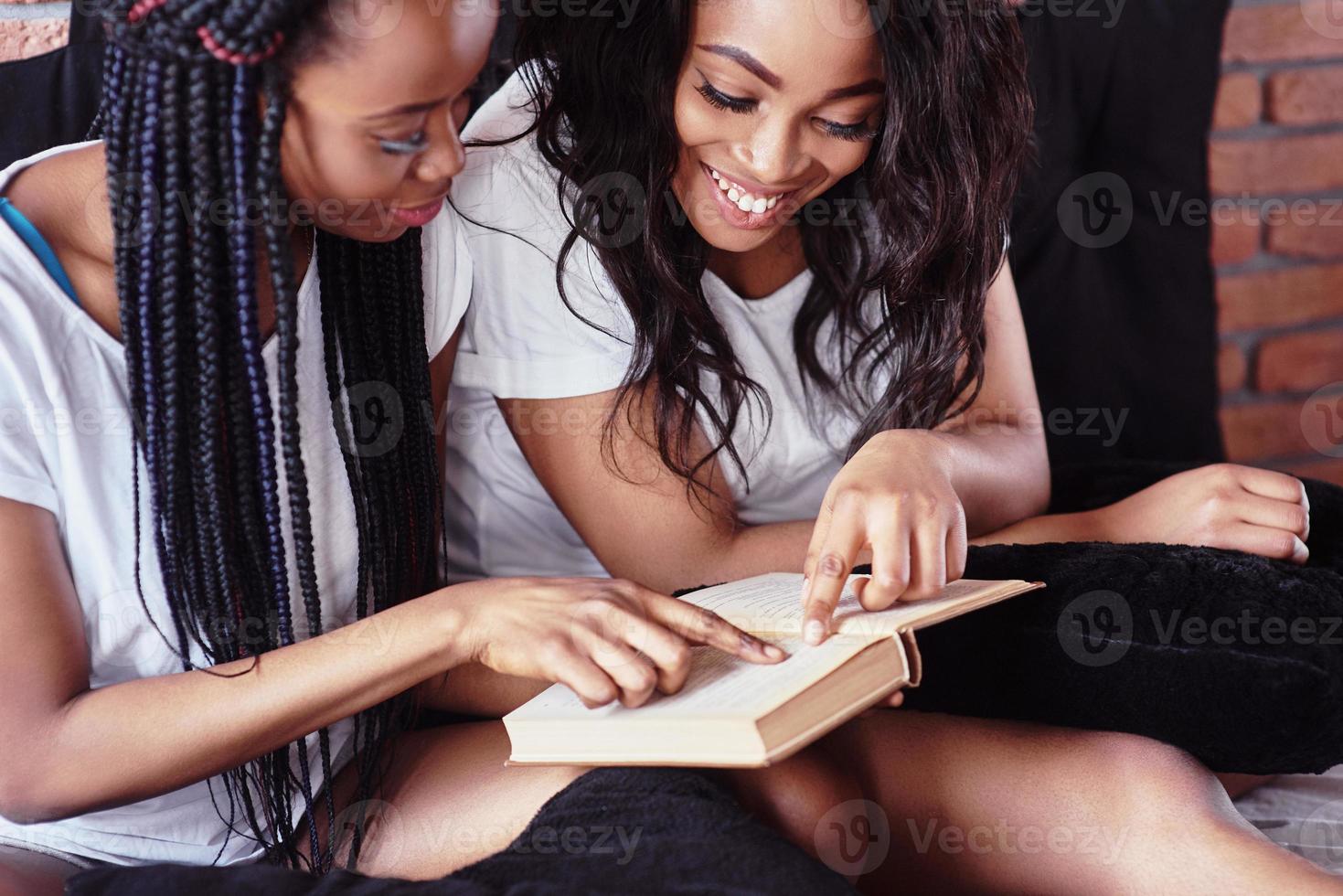 Two beautiful african girl in sleepwear smiling sitting on bed at home woke up in the morning on a sunny day. photo