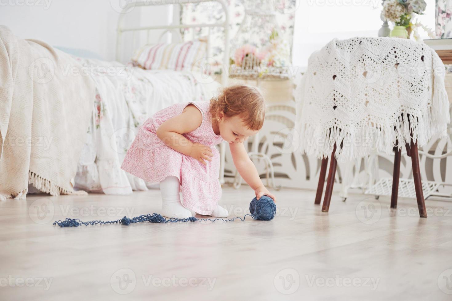 Childhood concept. Baby girl in cute dress play with colored thread. White vintage childroom photo