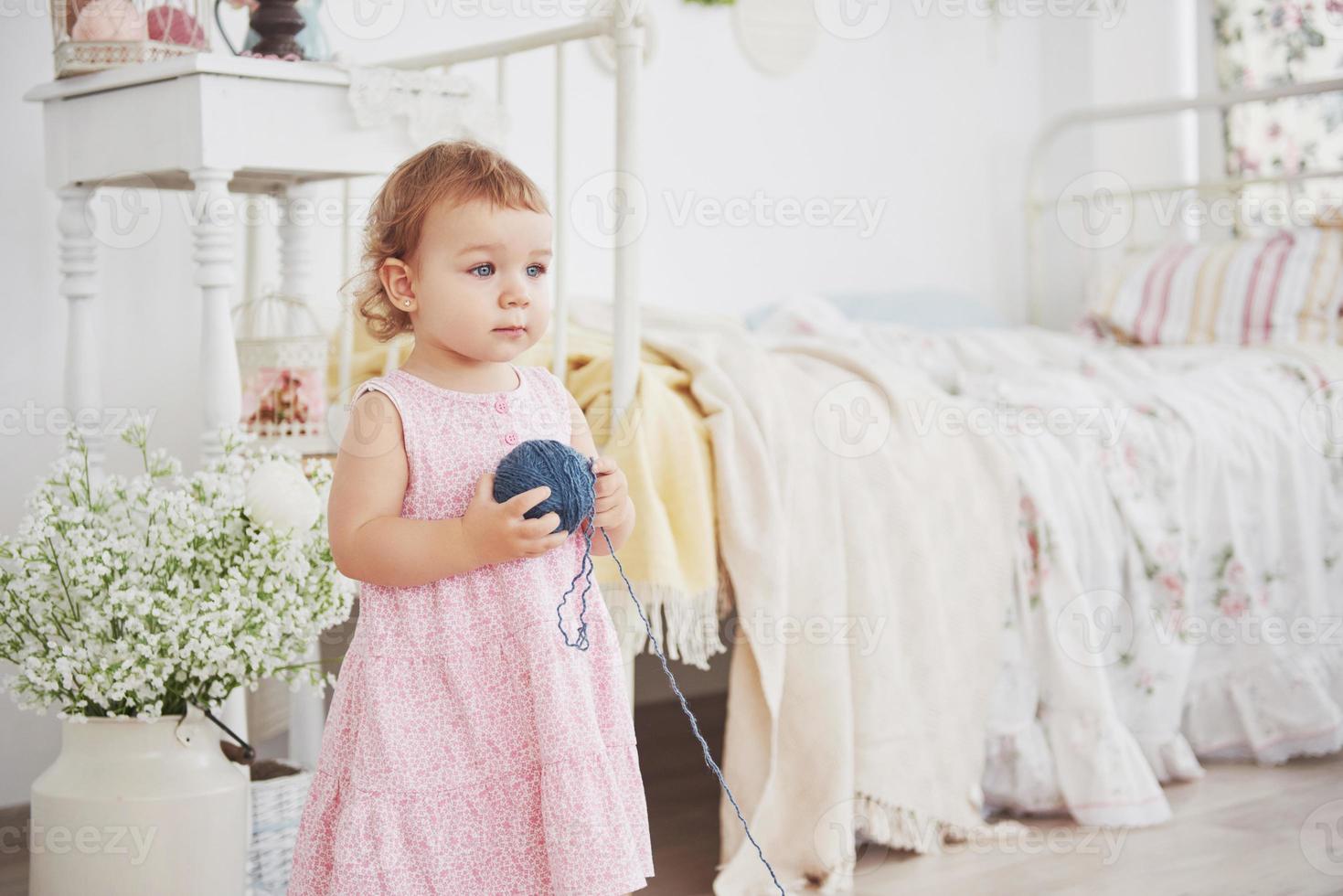 Childhood concept. Baby girl in cute dress play with colored thread. White vintage childroom photo