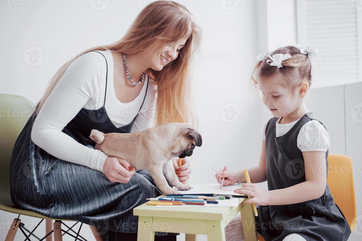 Los dibujos de madre e hija se dedican a la creatividad en el jardín de infantes. pequeño pug con ellos foto