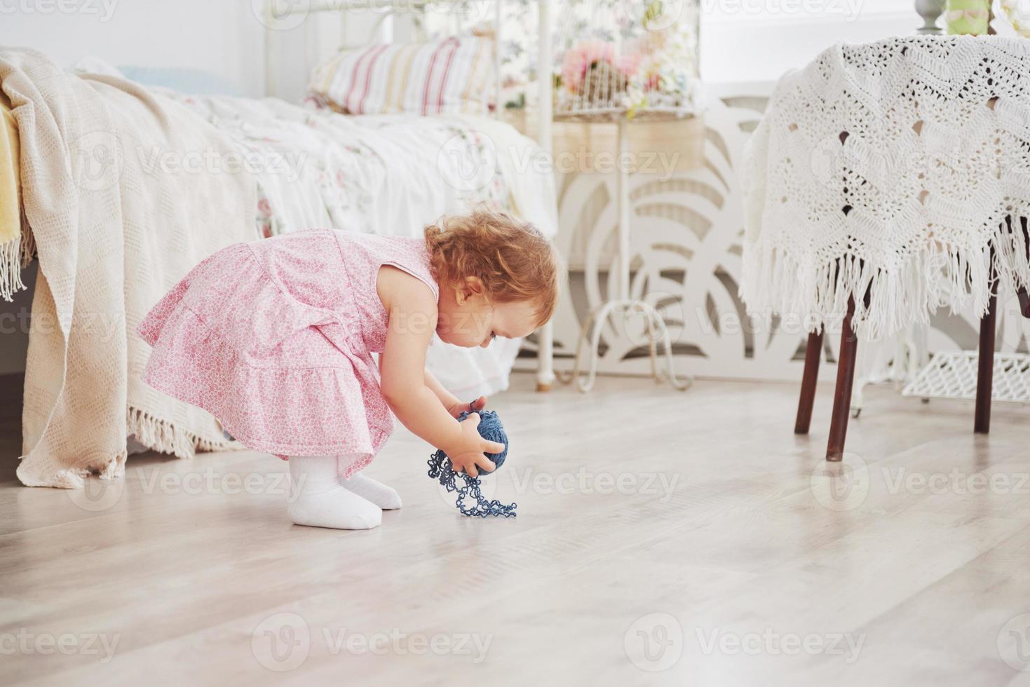 Childhood concept. Baby girl in cute dress play with colored thread. White vintage childroom photo