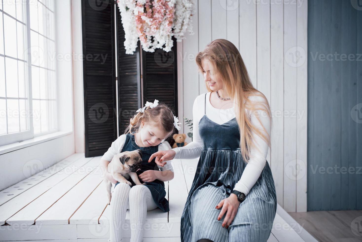 familia amorosa feliz. madre y su hija niña jugando y abrazando adorable pug foto