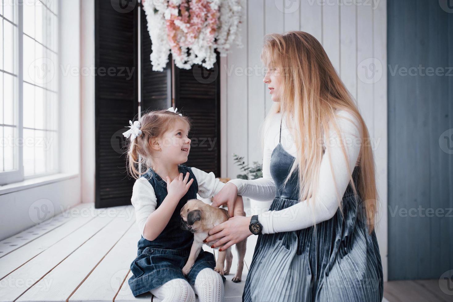 familia amorosa feliz. madre y su hija niña jugando y abrazando adorable pug foto