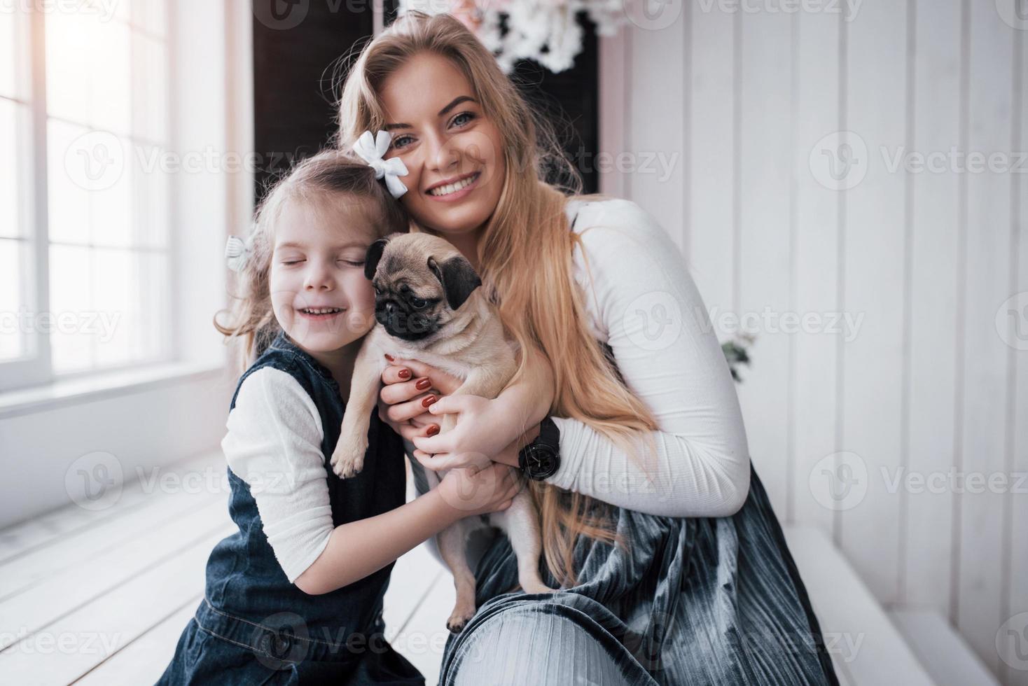 familia amorosa feliz. madre y su hija niña jugando y abrazando adorable pug foto