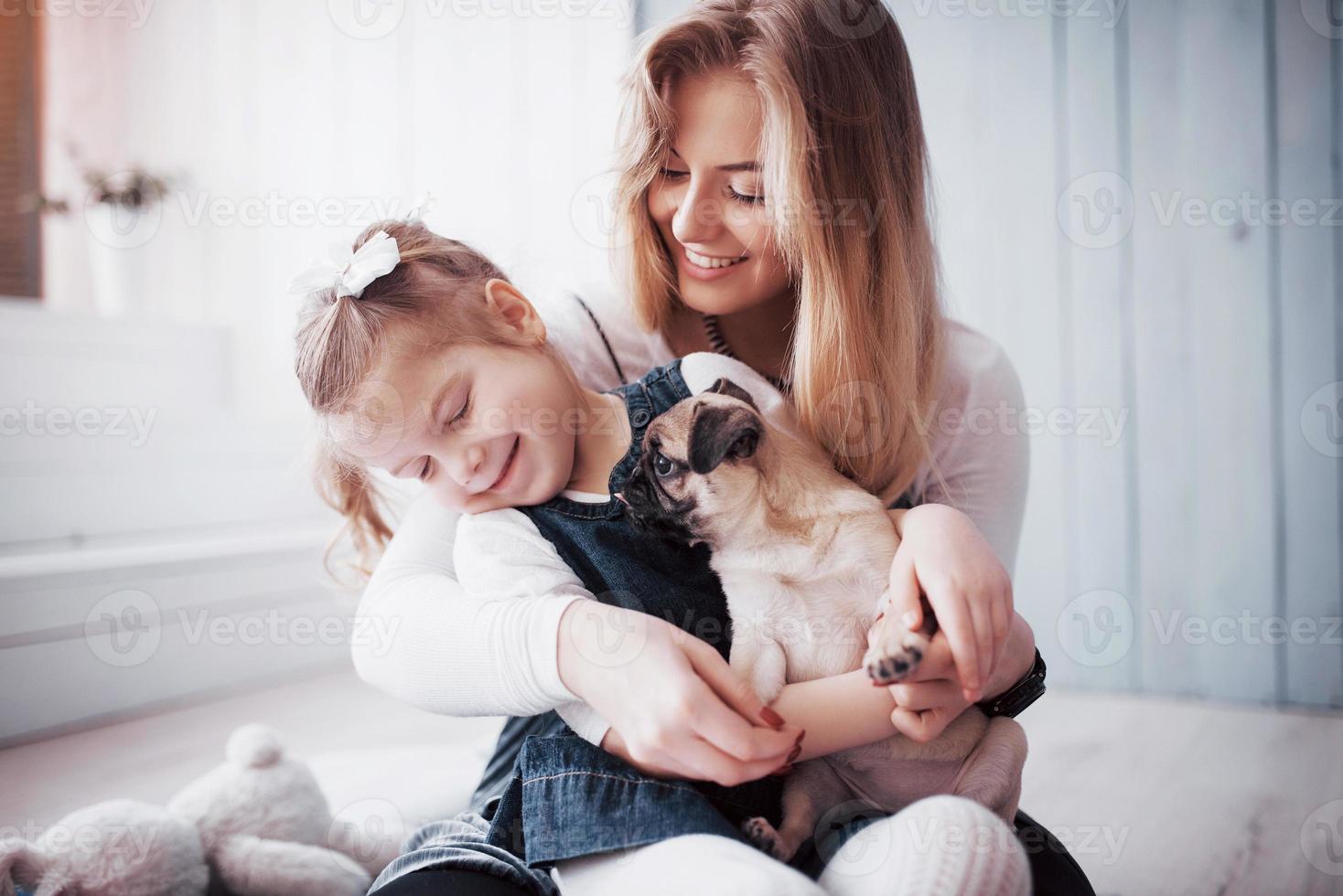 familia amorosa feliz. madre y su hija niña jugando y abrazando adorable pug foto