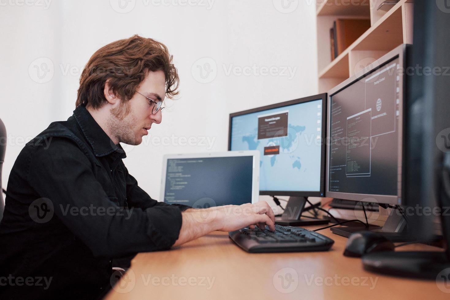The young dangerous hacker breaks down government services by downloading sensitive data and activating viruses. A man uses a laptop computer with many monitors photo