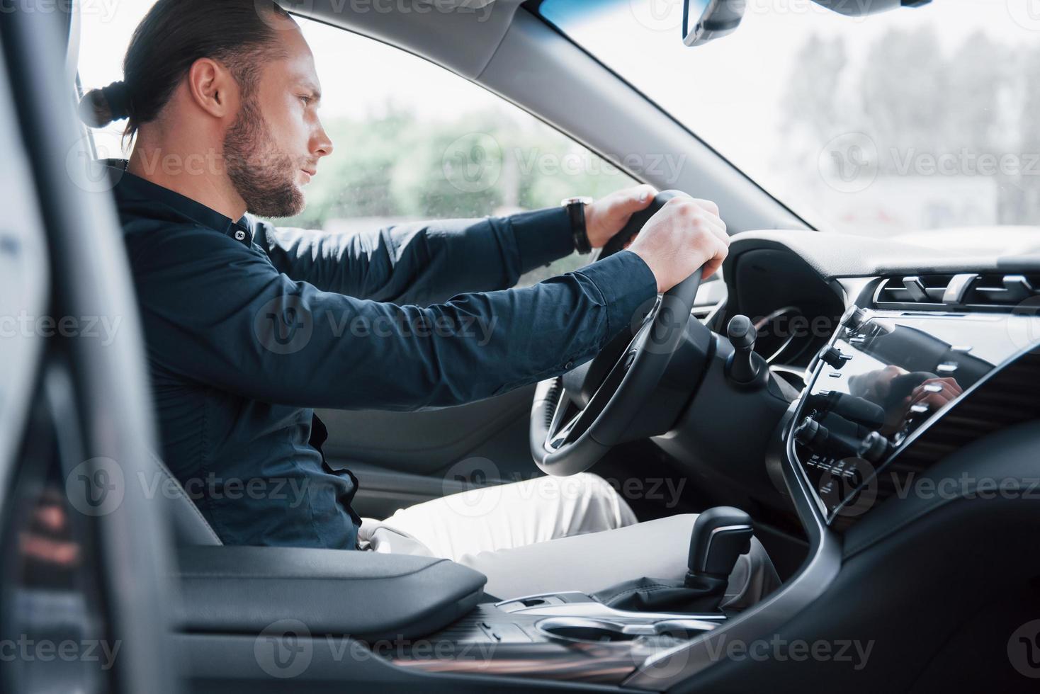 Confident young businessman sitting at the wheel of his new car photo