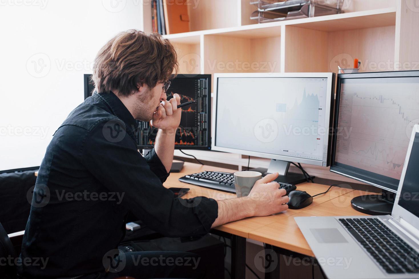 Stressful day at the office. Young businessman holding hands on his face while sitting at the desk in creative office. Stock Exchange Trading Forex Finance Graphic Concept photo
