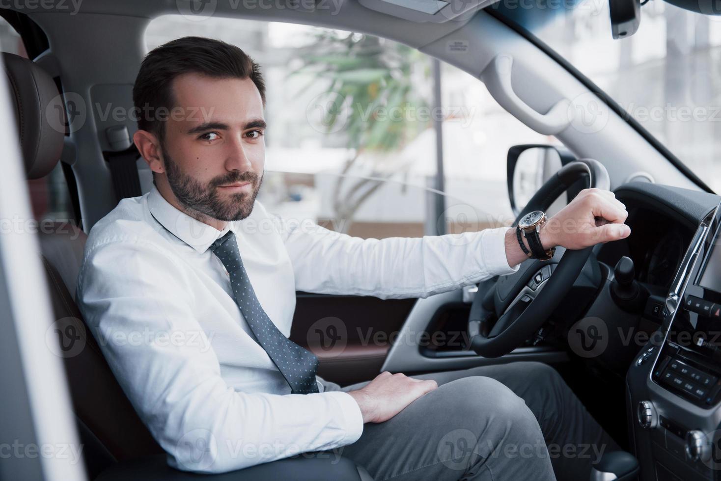 Confiado joven empresario sentado al volante de su coche nuevo foto