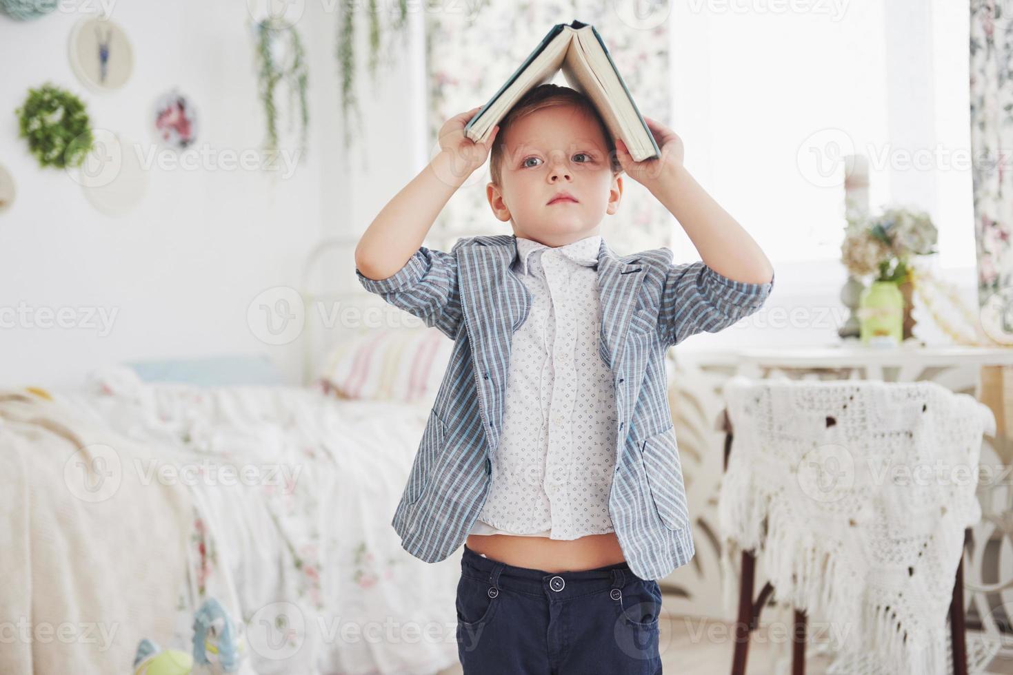 Photo of diligent schoolboy with book on his head doing homework. The schoolboy is tired of doing homework