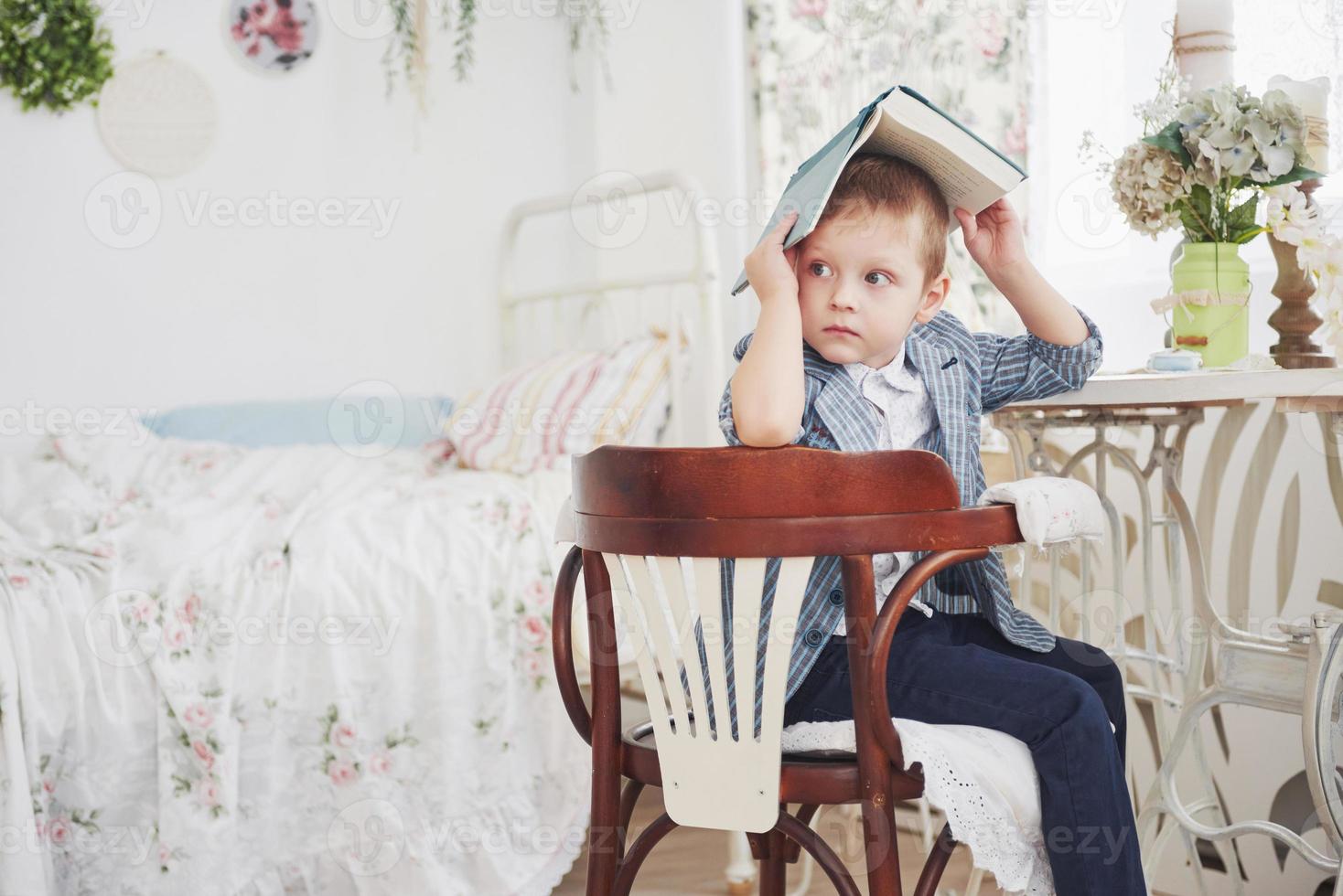 Photo of diligent schoolboy with book on his head doing homework. The schoolboy is tired of doing homework