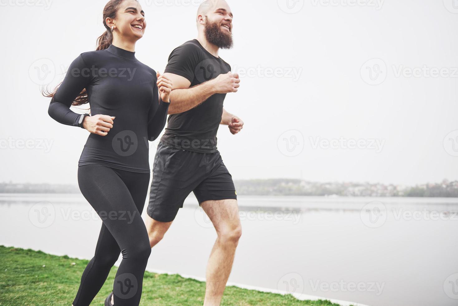 Couple jogging and running outdoors in park near the water. Young bearded man and woman exercising together in morning photo