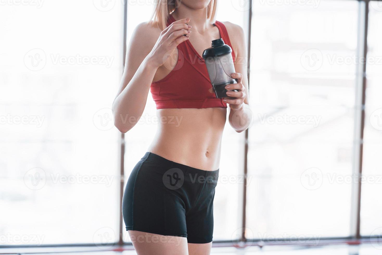 Foto de atractiva mujer fitness en el gimnasio y sosteniendo una botella de agua