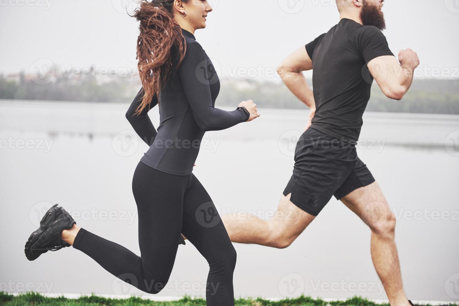 Couple jogging and running outdoors in park near the water. Young bearded man and woman exercising together in morning photo