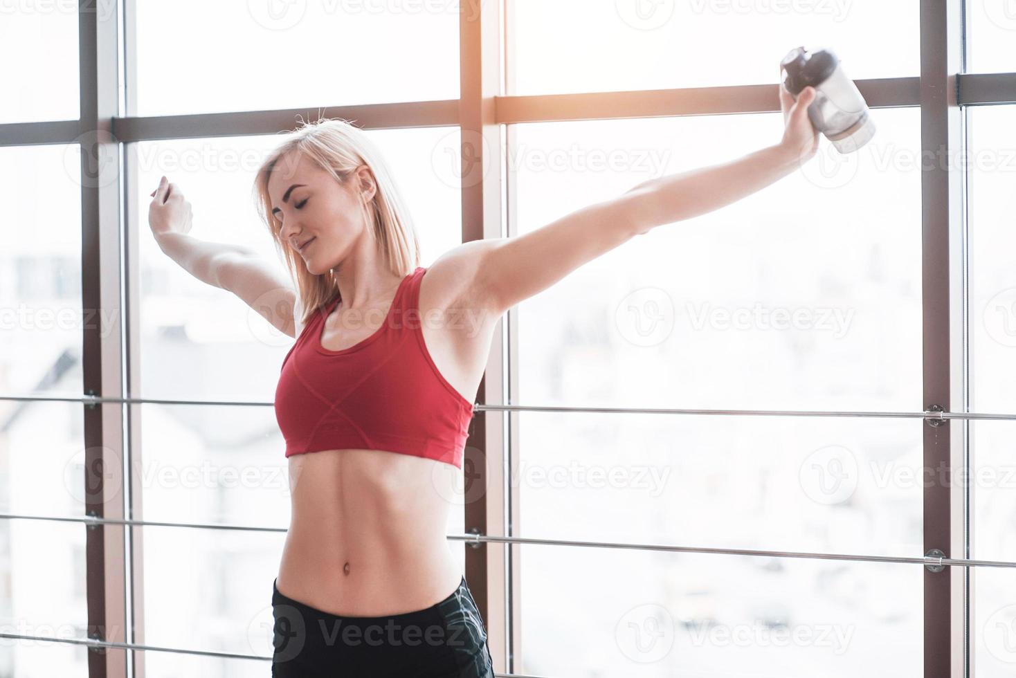 Foto de atractiva mujer fitness en el gimnasio y sosteniendo una botella de agua