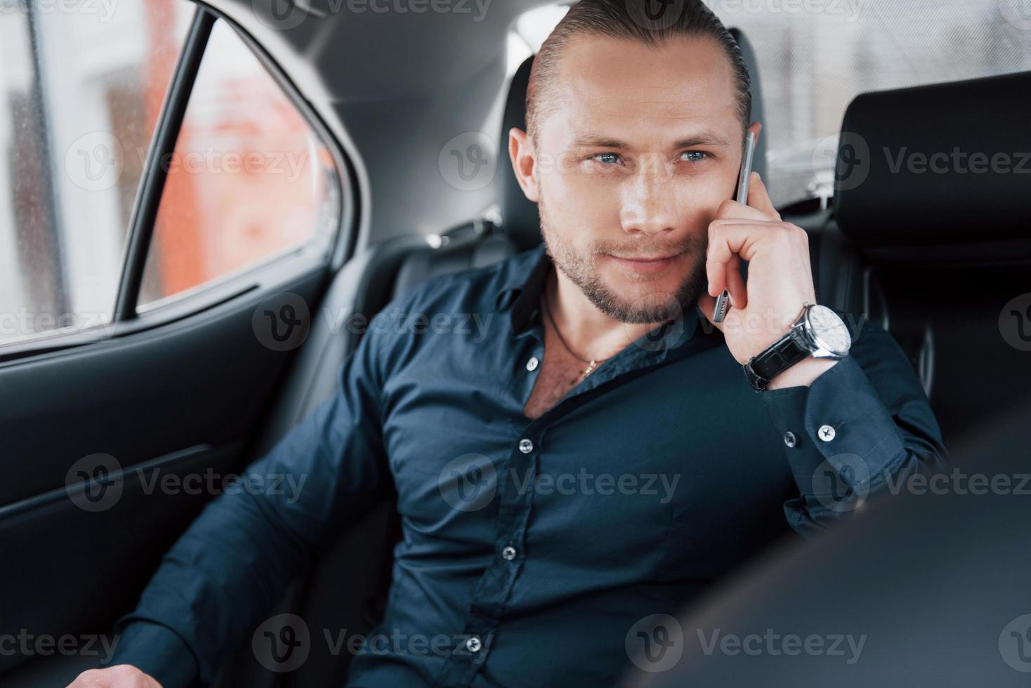 A modern businessman speaks on the phone in the back of the car photo