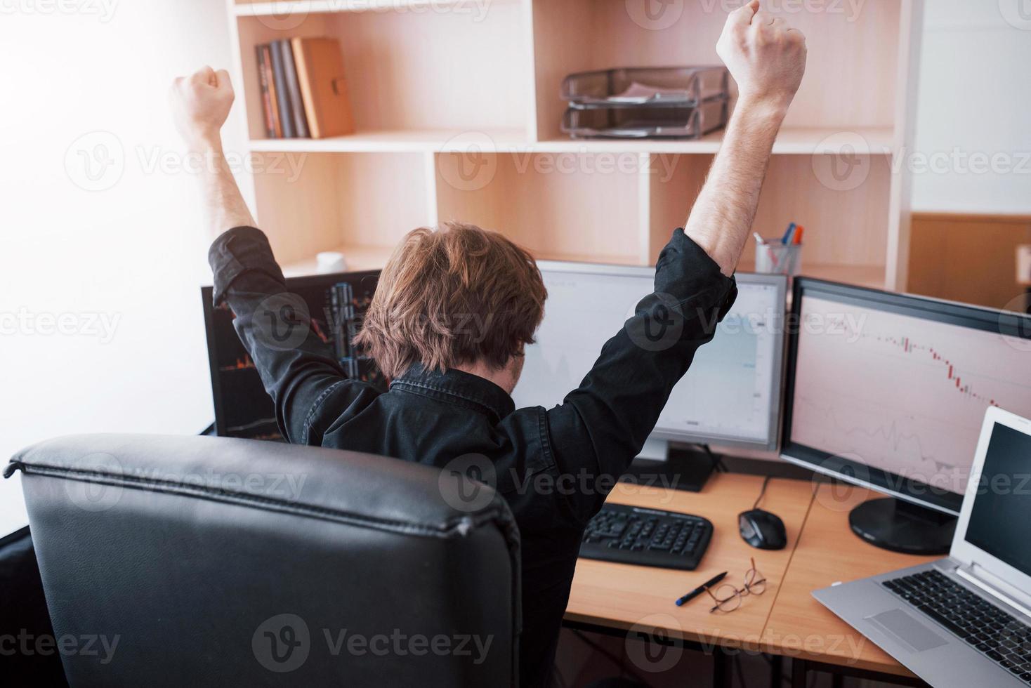 corredor de bolsa joven que estira las manos en el lugar de trabajo, primero logró un gran éxito en el mercado de valores foto