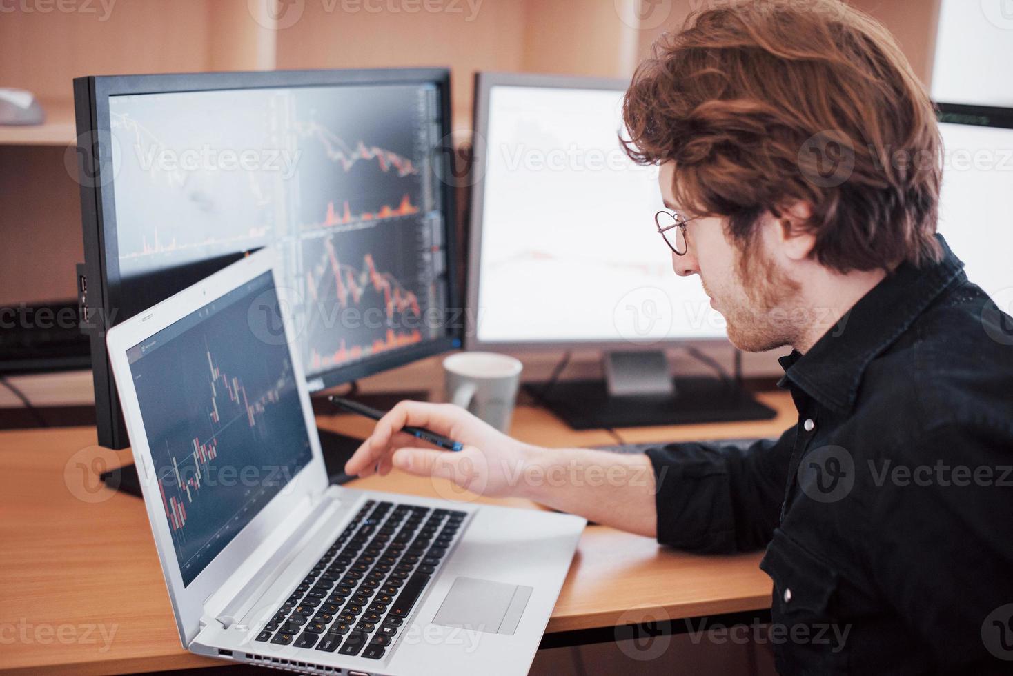 Stressful day at the office. Young businessman holding hands on his face while sitting at the desk in creative office. Stock Exchange Trading Forex Finance Graphic Concept photo