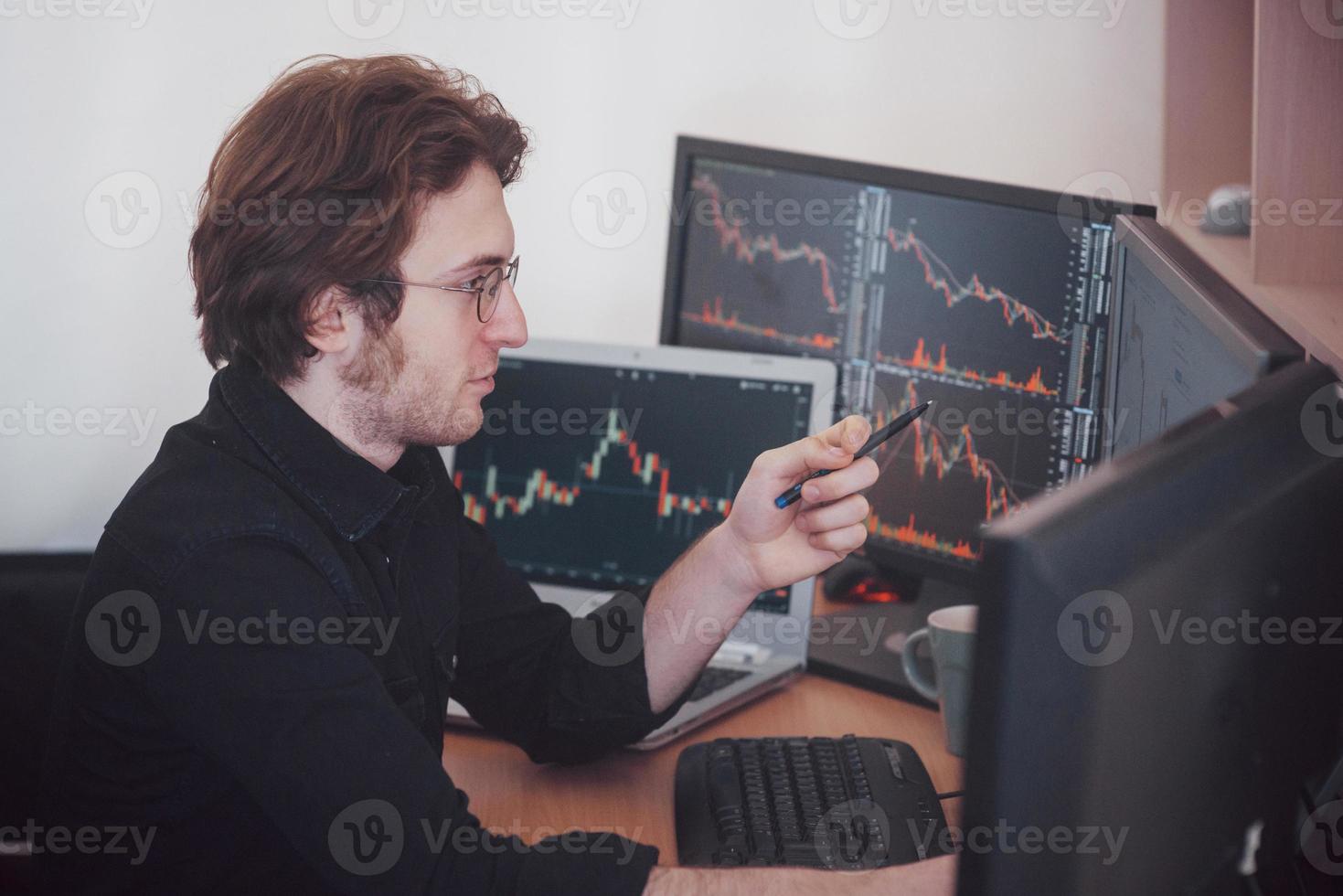 Stressful day at the office. Young businessman holding hands on his face while sitting at the desk in creative office. Stock Exchange Trading Forex Finance Graphic Concept photo