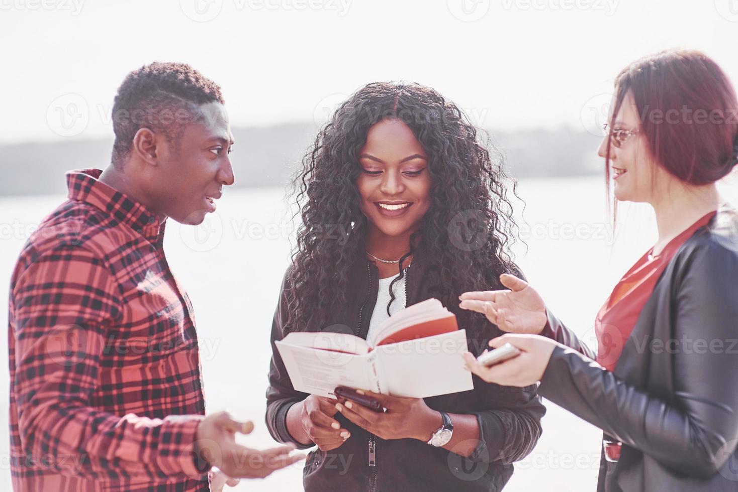 Un grupo de jóvenes multinacionales con un libro, estudiantes que estudian al aire libre. foto