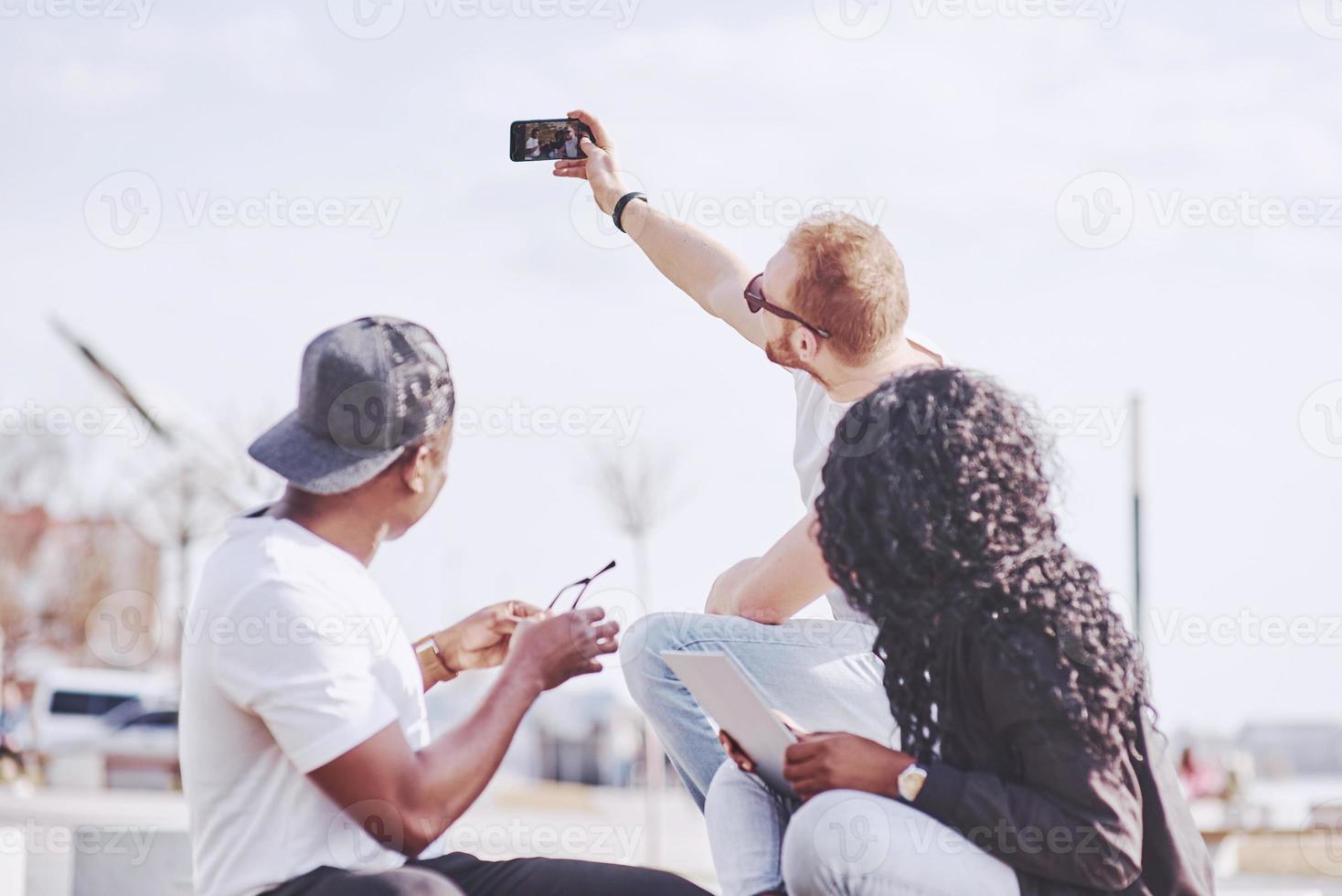 Beautiful multi ethnic friends using a laptop in the Street and make selphie. Youth lifestyle concept photo