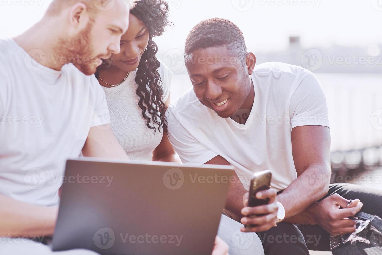 hermosos amigos multiétnicos usando una computadora portátil en la calle. concepto de estilo de vida juvenil foto