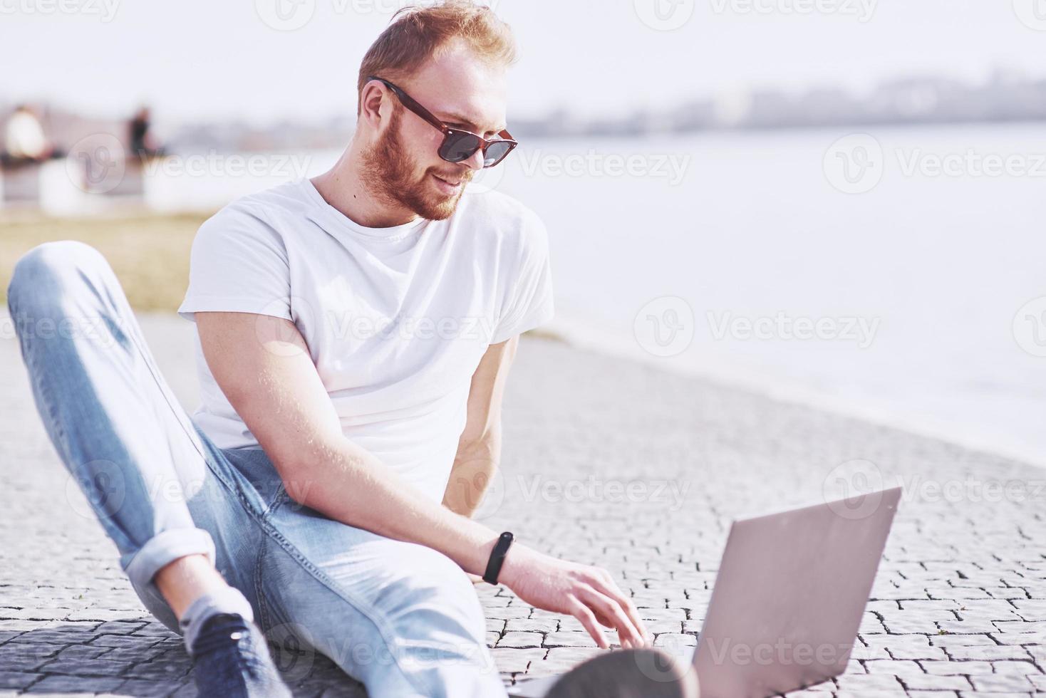 Young man sitting with laptop outside the office. Student learning online. Summer sunny day photo