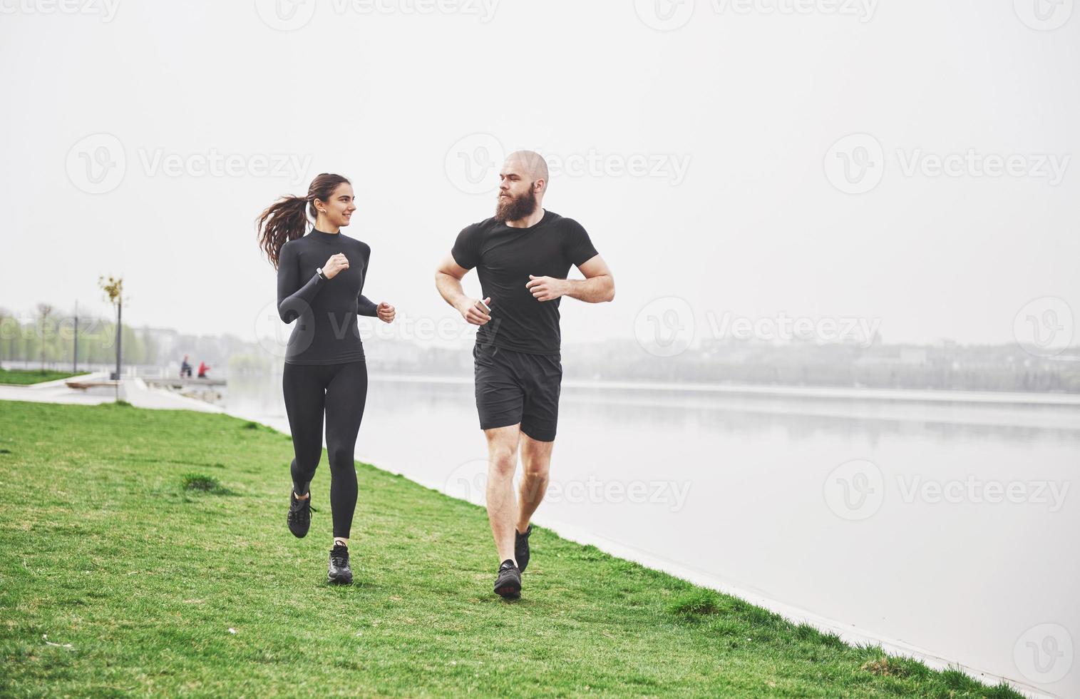 Couple jogging and running outdoors in park near the water. Young bearded man and woman exercising together in morning photo