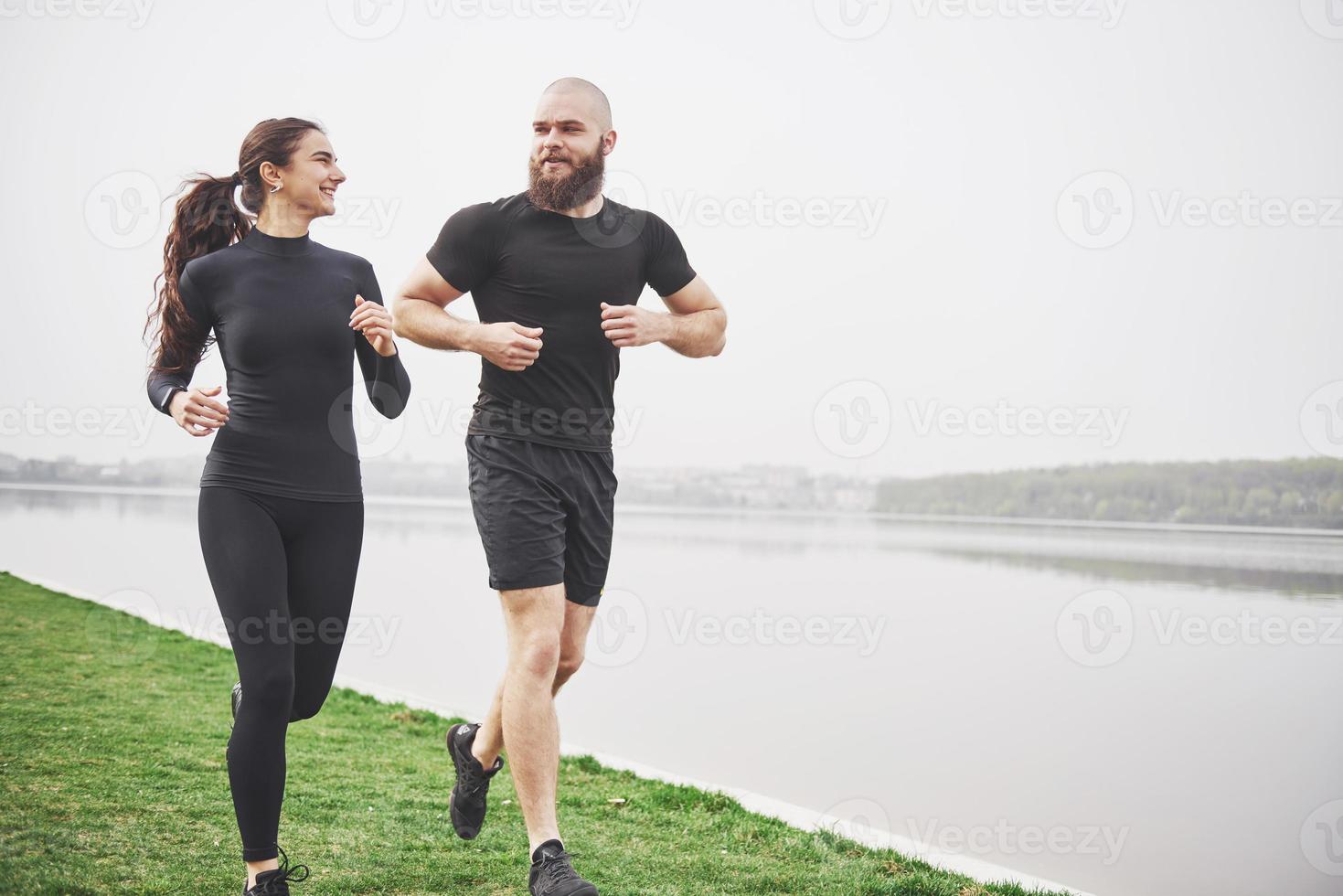 Couple jogging and running outdoors in park near the water. Young bearded man and woman exercising together in morning photo