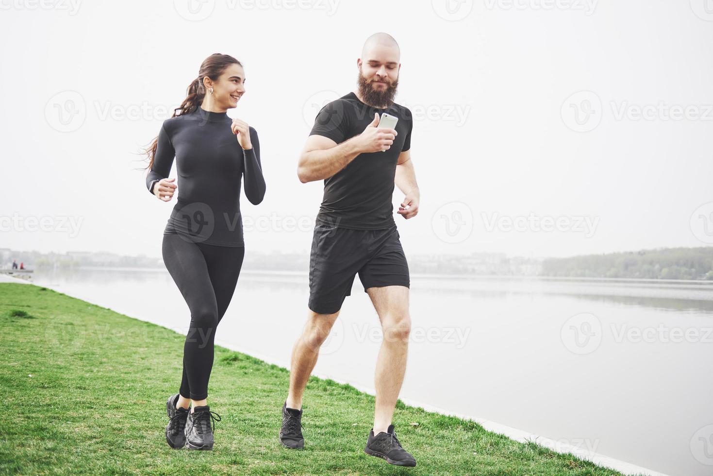 Couple jogging and running outdoors in park near the water. Young bearded man and woman exercising together in morning photo