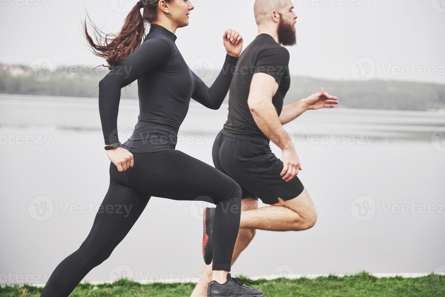 Couple jogging and running outdoors in park near the water. Young bearded man and woman exercising together in morning photo