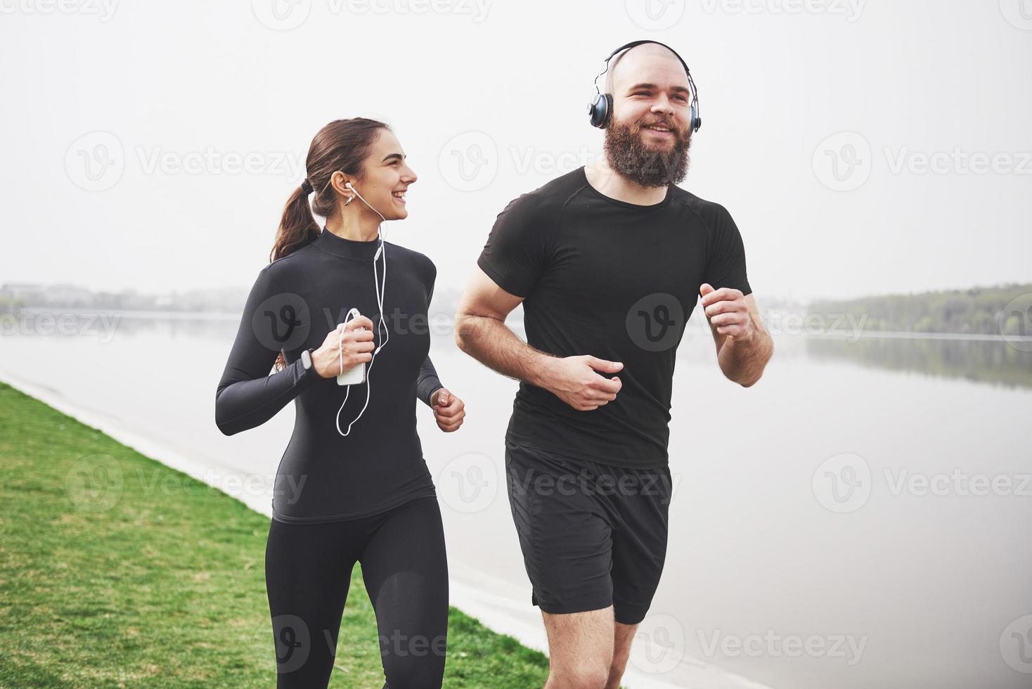 Couple jogging and running outdoors in park near the water. Young bearded man and woman exercising together in morning photo
