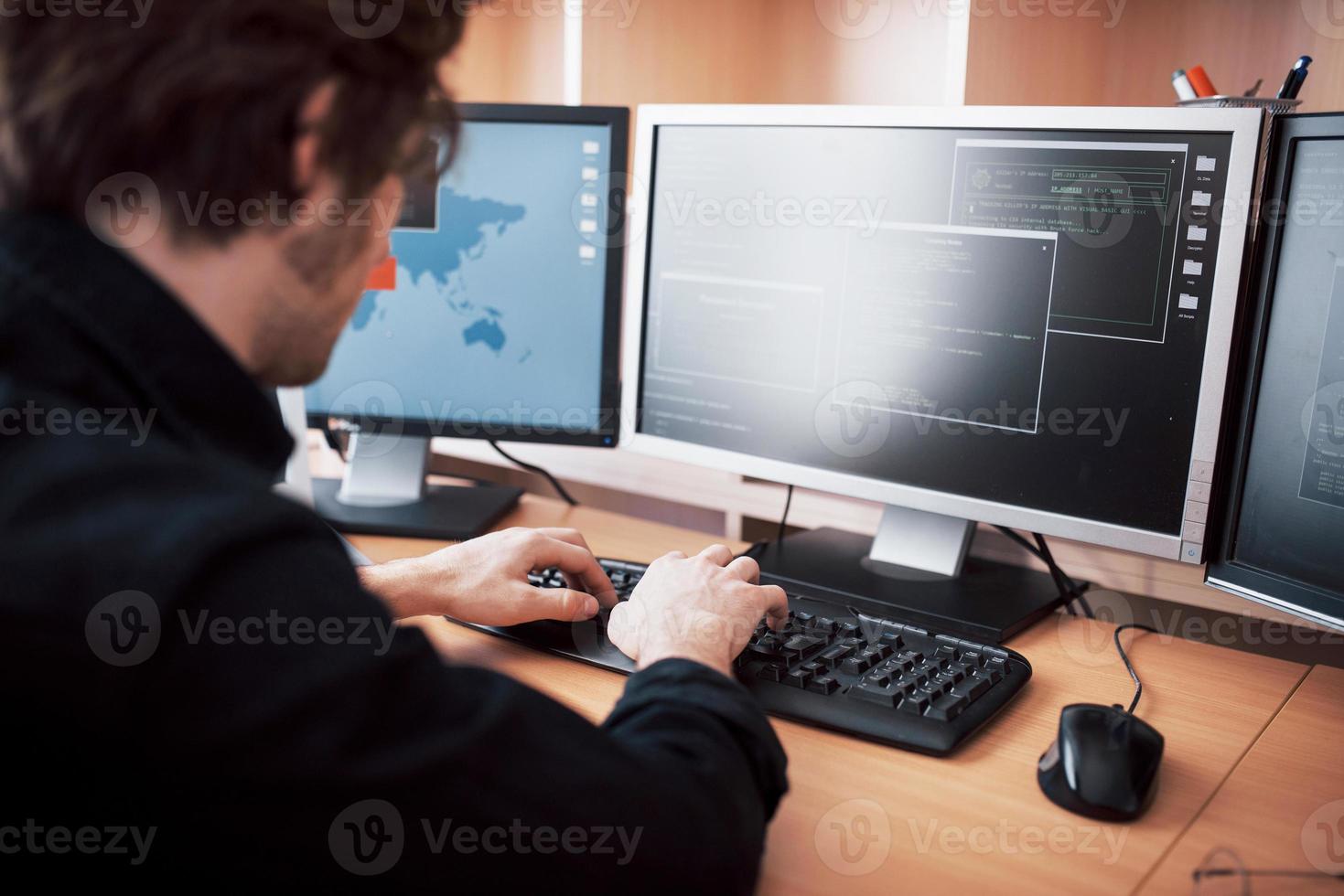 The young dangerous hacker breaks down government services by downloading sensitive data and activating viruses. A man uses a laptop computer with many monitors photo