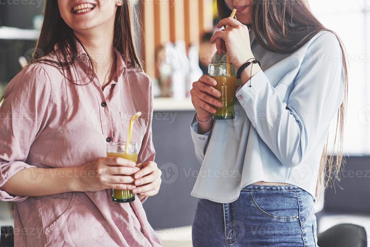 dos hermosas gemelas pasan tiempo bebiendo jugo. hermanas relajándose en un café y divirtiéndose juntas foto