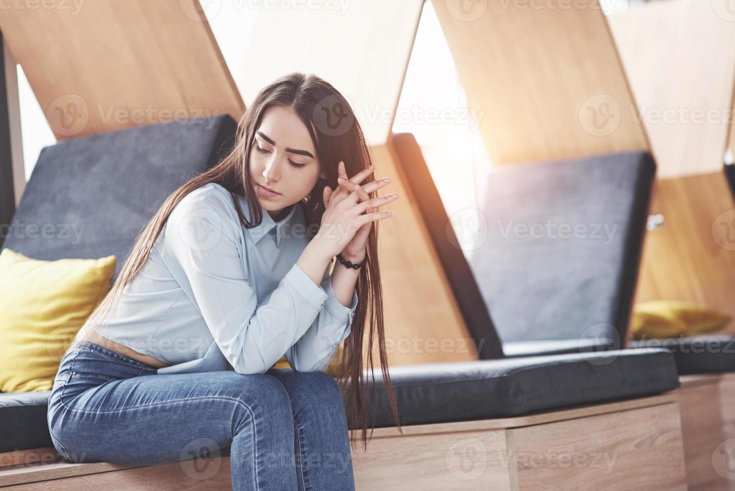 Beautiful young girl spends her time in the recreation area. She sits and has fun in the sofa chair in the form of a hexagon with pillows near the window photo