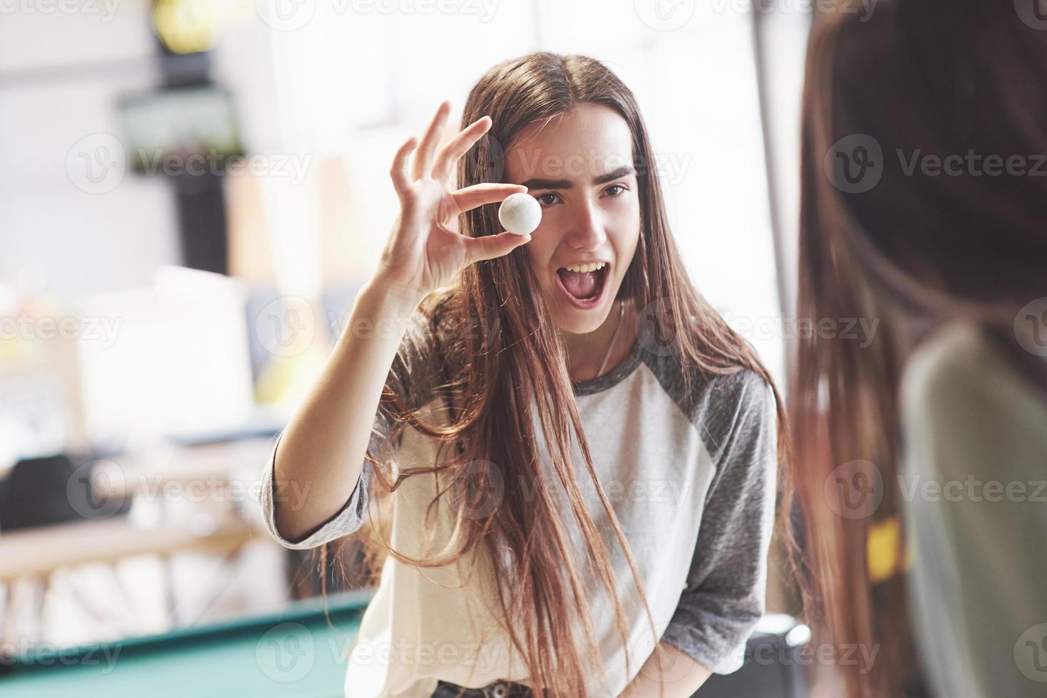 dos hermosas niñas gemelas juegan al futbolín y se divierten. una de las hermanas sostiene una pelota de juguete en su mano y se ríe foto