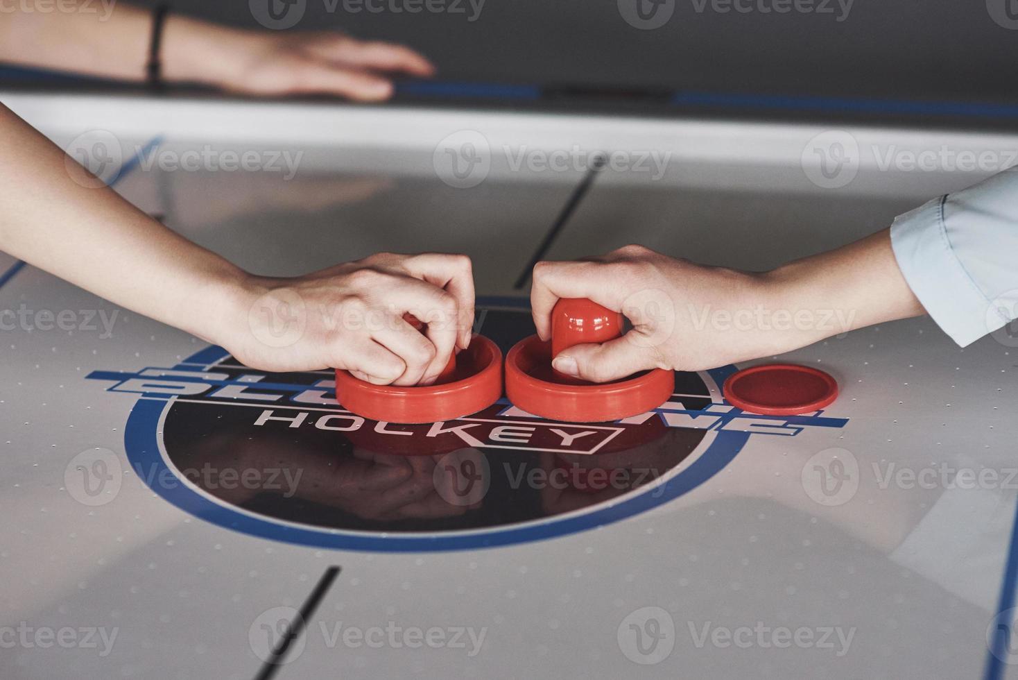 Manos de jóvenes sosteniendo el delantero en la mesa de hockey de aire en la sala de juegos foto