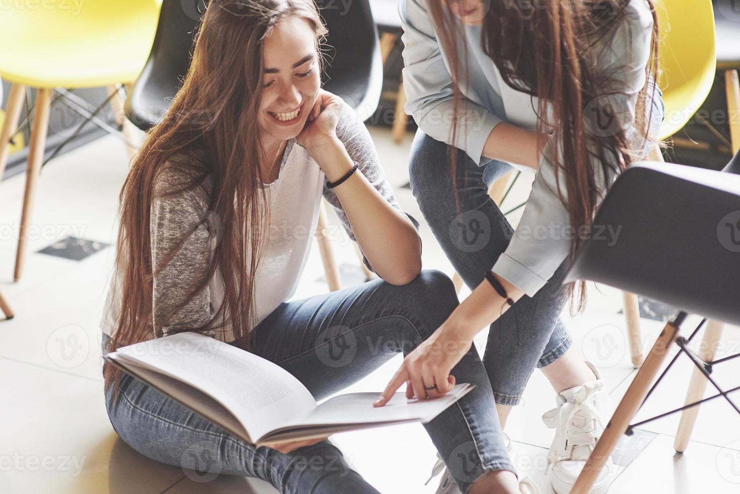 dos hermosas niñas gemelas pasan tiempo leyendo un libro en la biblioteca por la mañana. hermanas relajándose en un café y divirtiéndose juntas foto