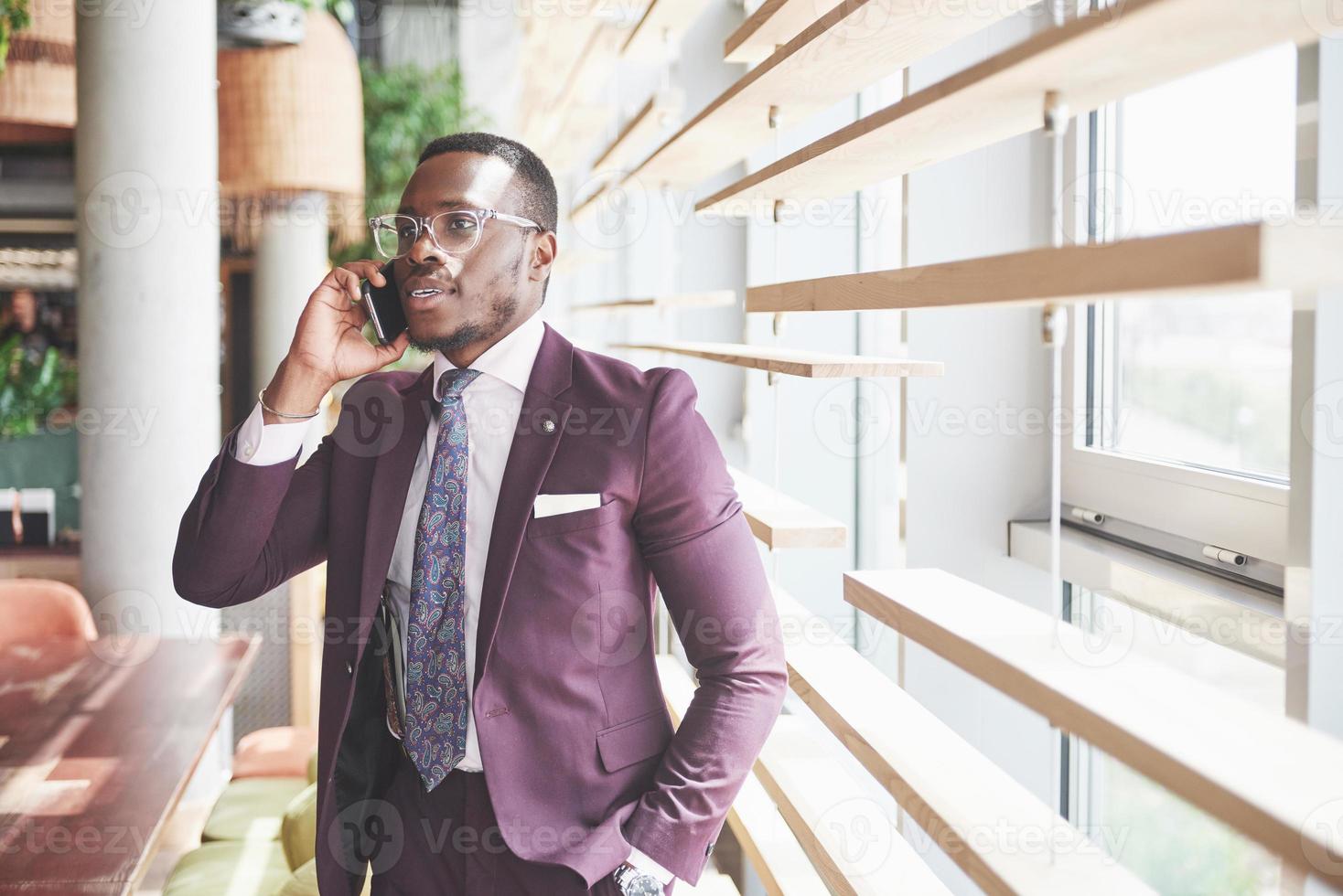 Retrato de un joven y guapo empresario afroamericano hablando en un traje por teléfono foto